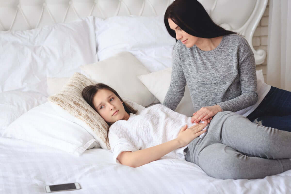 An adolescent teen lying in bed with her hand on her abdomen, and her mother comforting her. She'll stop growing soon.