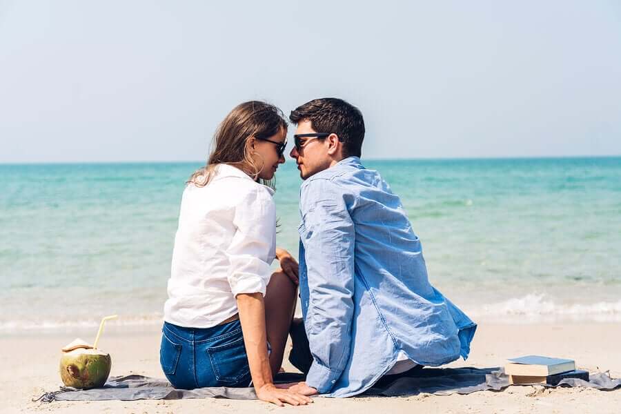 A couple sitting on the beach looking into one another's eyes.