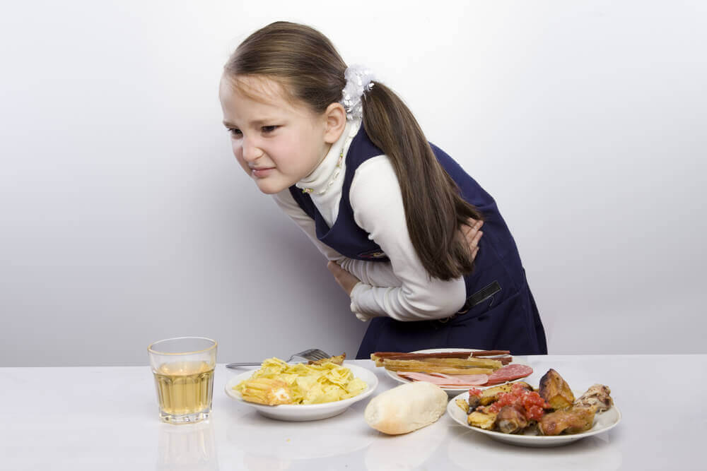 A young girl bent over in pain in front of a table of food.