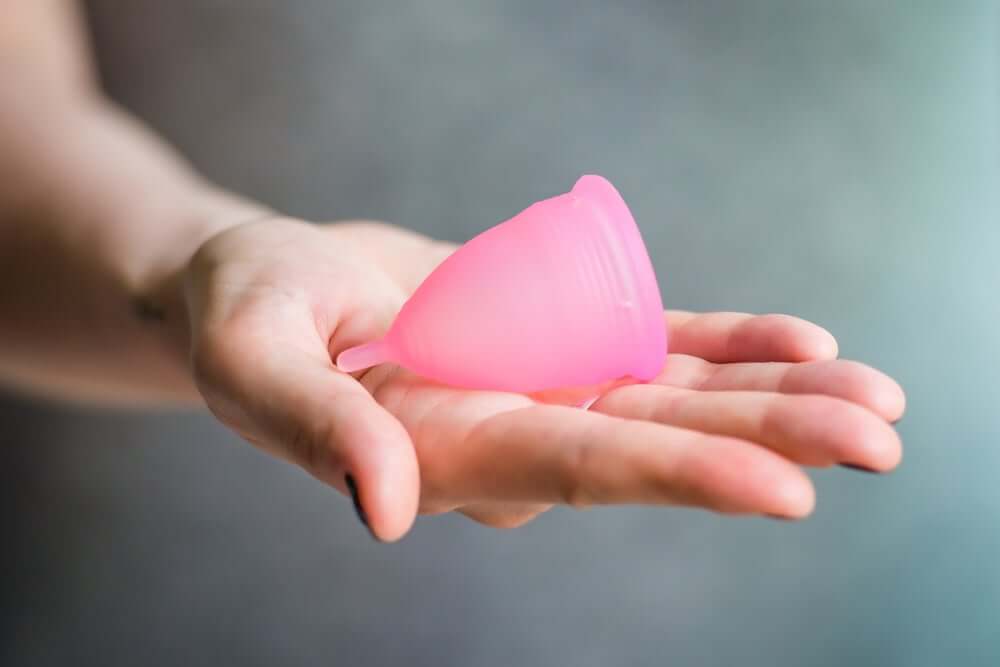 En kvinnes hånd som holder en rosa menstruasjonskopp.