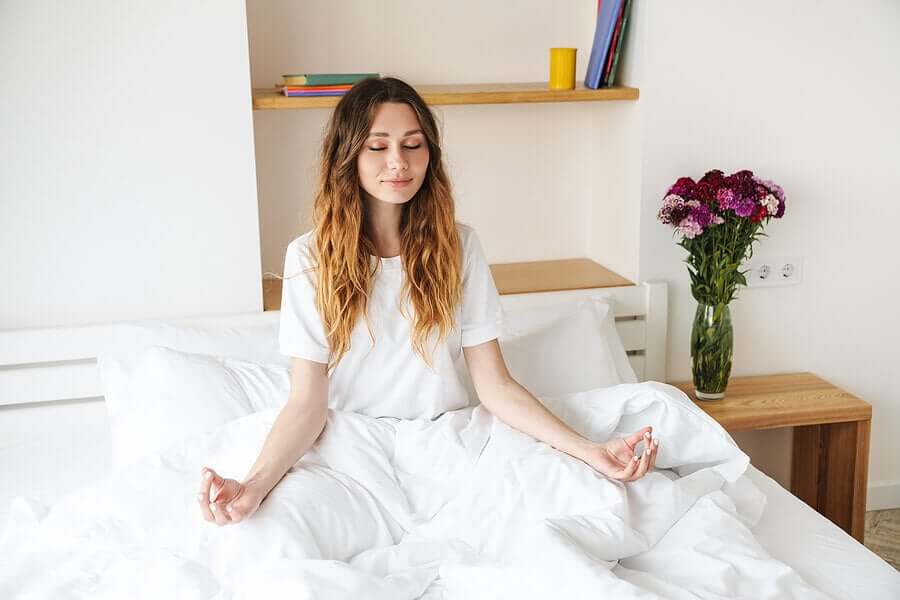 A woman meditating and smiling peacefully in bed.