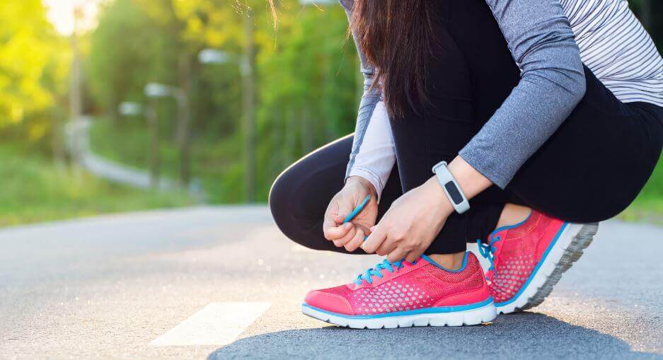 A woman kneeling down to tie her tennis shoes.