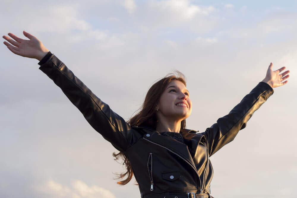 A young woman smiling with her hands in the air.
