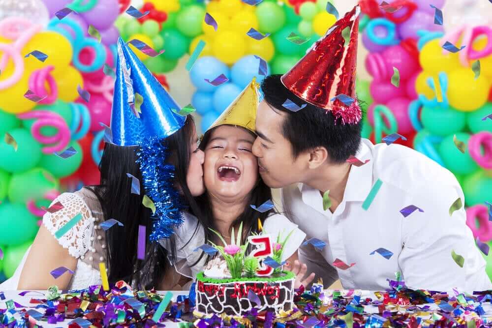 Forældre kysser deres datter på kinden under hendes fødselsdagsfest