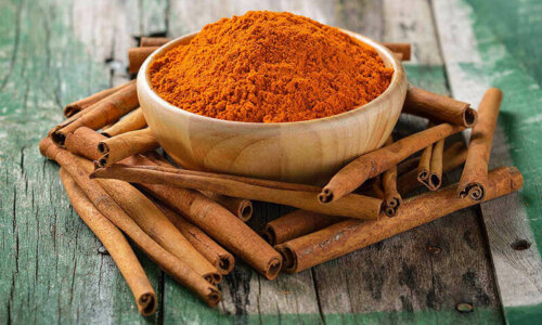 Skål med stødt kanel på et træbord med kanelstænger