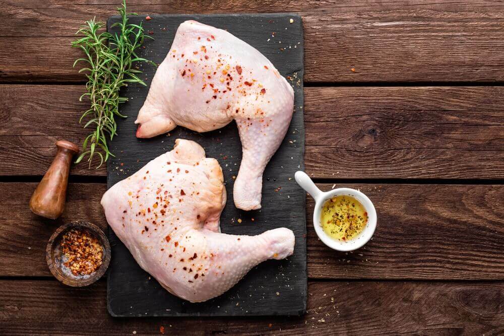 Raw chicken on a cutting board with olive oil, spices, and herbs.