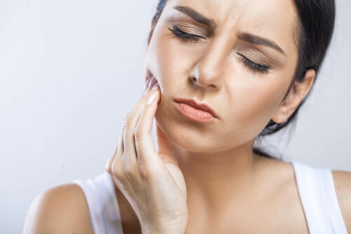 woman with touching her cheek in pain to indicate painful tooth