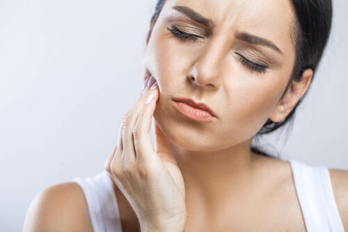 kvinne med å berøre kinnet hennes i smerte for å indikere smertefull tann