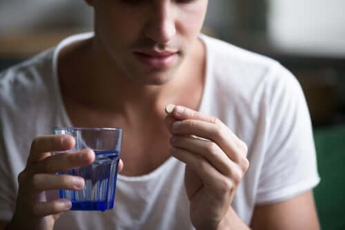 En person, der holder en pille og et glas vand