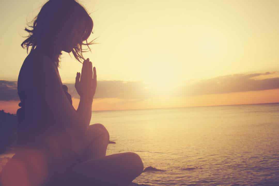 Gün batımında sahilde meditasyon yapan bir kadın.