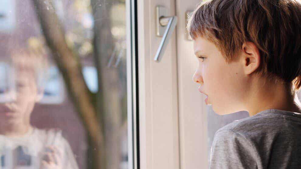 Dziecko z autyzmem wygląda przez okno.