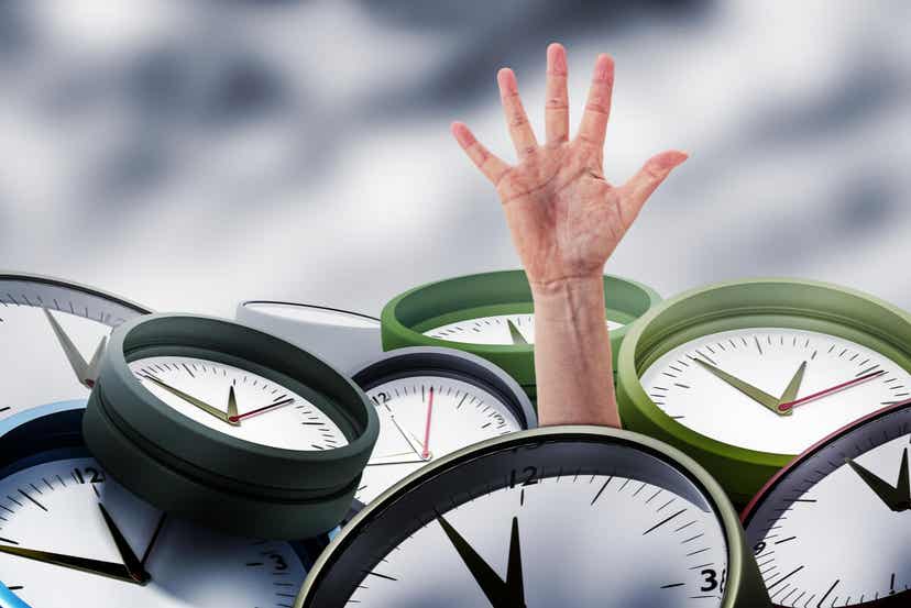 A hand reaching out from under a pile of clocks.