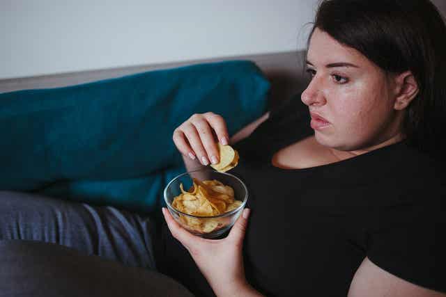 A woman eating a snack on the couch.