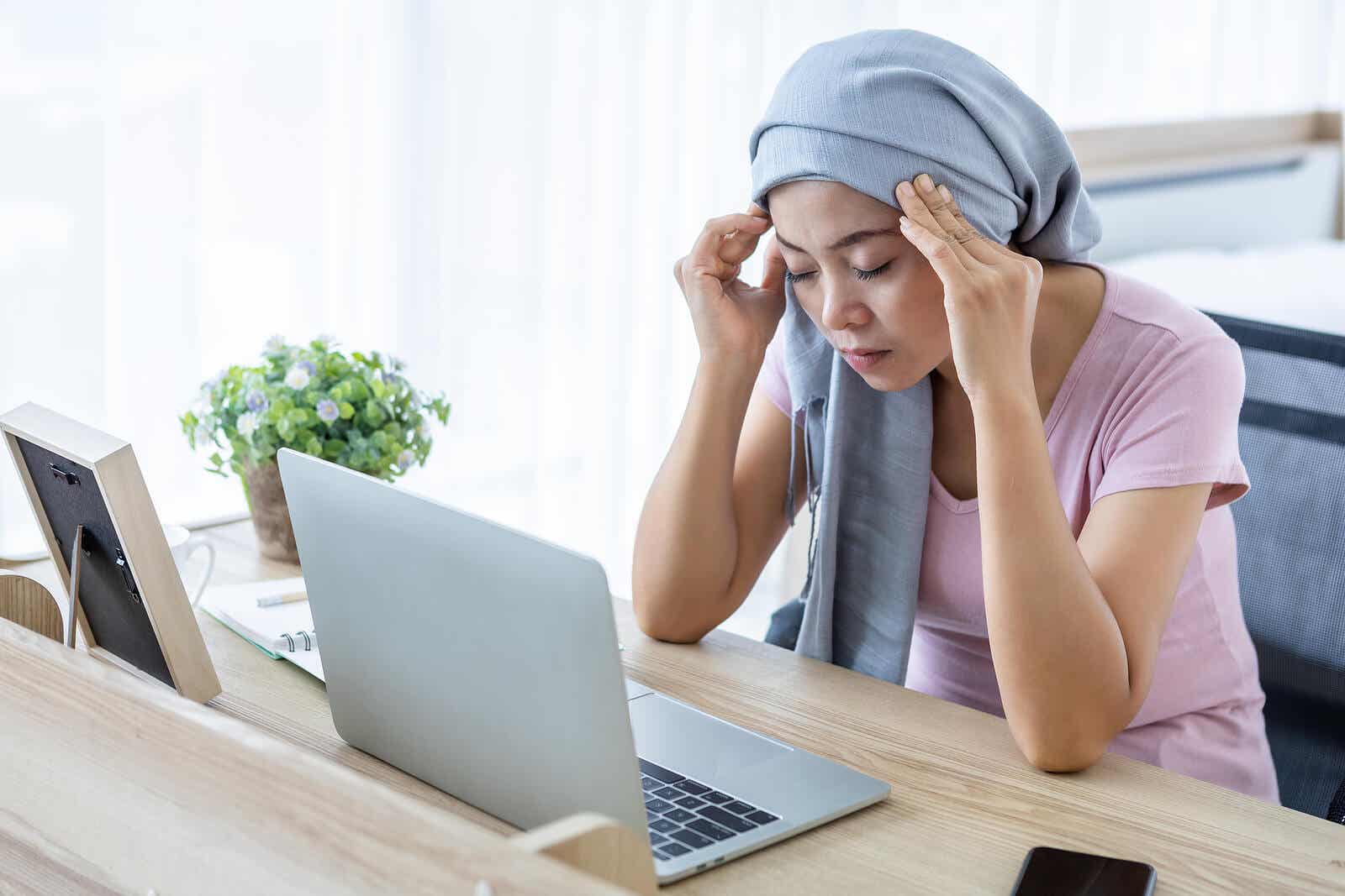 A woman sitting at her laptop with a scarf around her head, rubbing her temples.