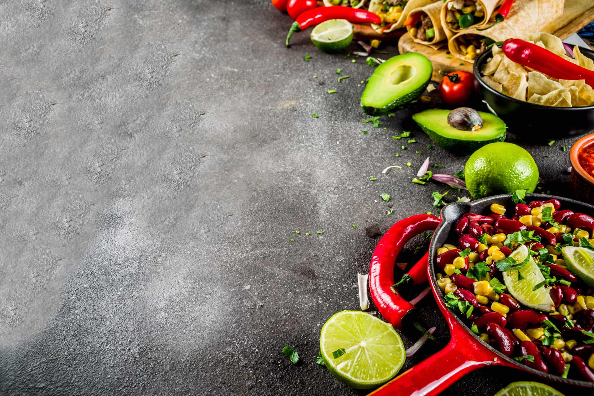 A skillet, bowl, and cutting board, all full of fresh Mexican foods made of beans, fruits, and vegetables.