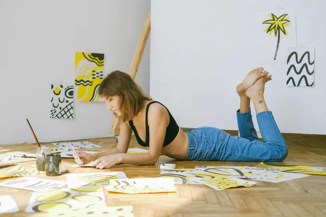 A woman lying on the floor painting, alone.