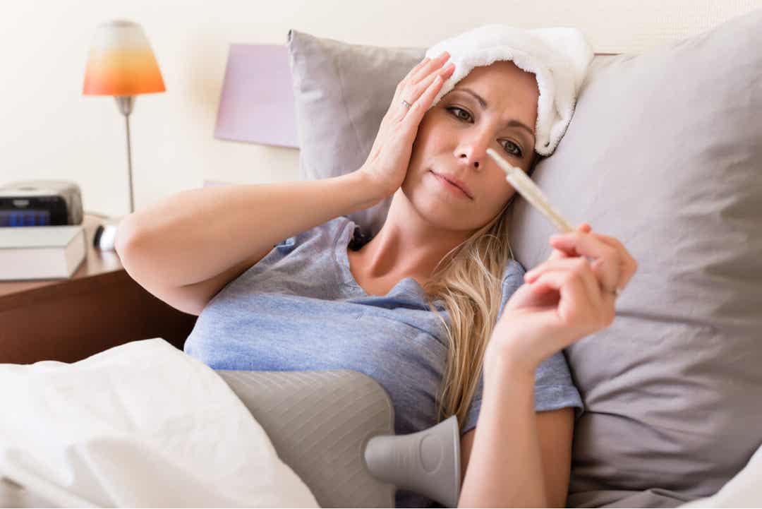 A woman lying in bed with a fever, taking her temperature.