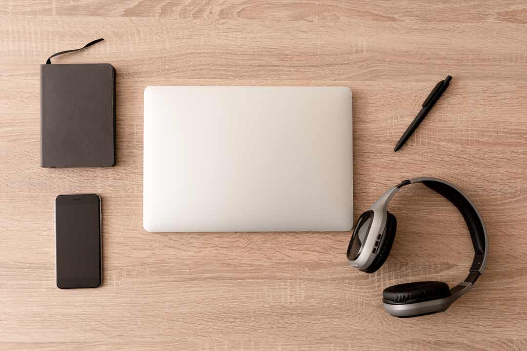 Ein Planer, ein Smartphone, ein Laptop, ein Stift und Kopfhörer, ordentlich angeordnet auf einem Desktop.