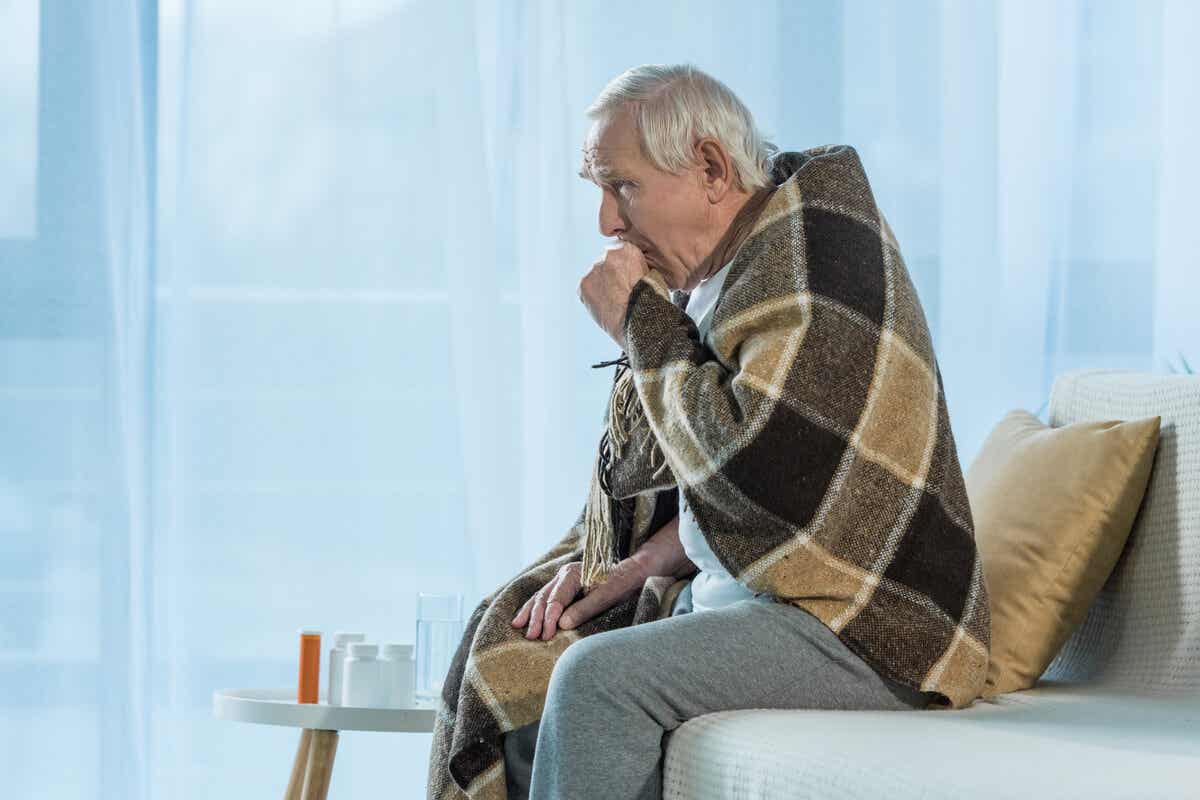 En ældre mand med et tæppe over skuldrene hoster i hånden