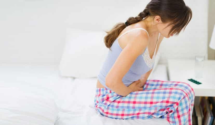A woman sitting on the edge of her bed with abdominal pain.