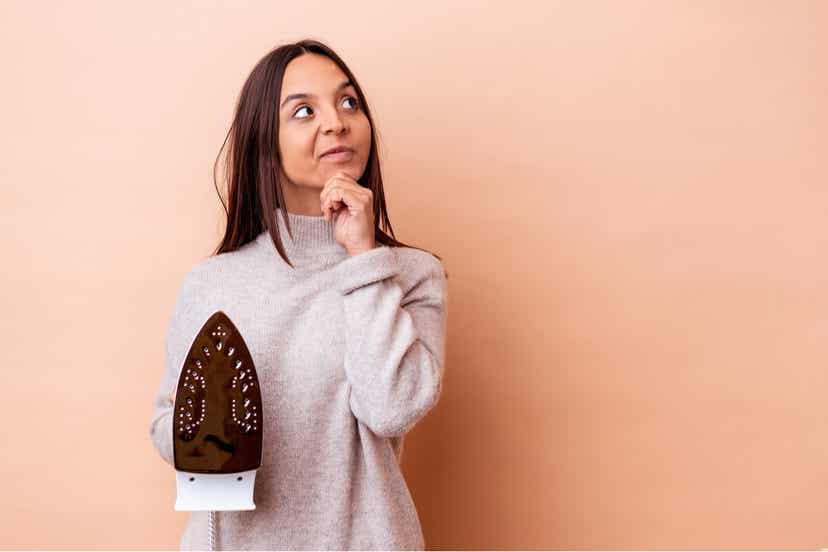 A woman holding an iron and thinking.