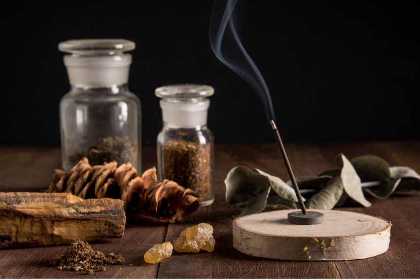 An incense burner surrounded by different objects from nature, including amber, a eucalyptus branch, and a pine cone.