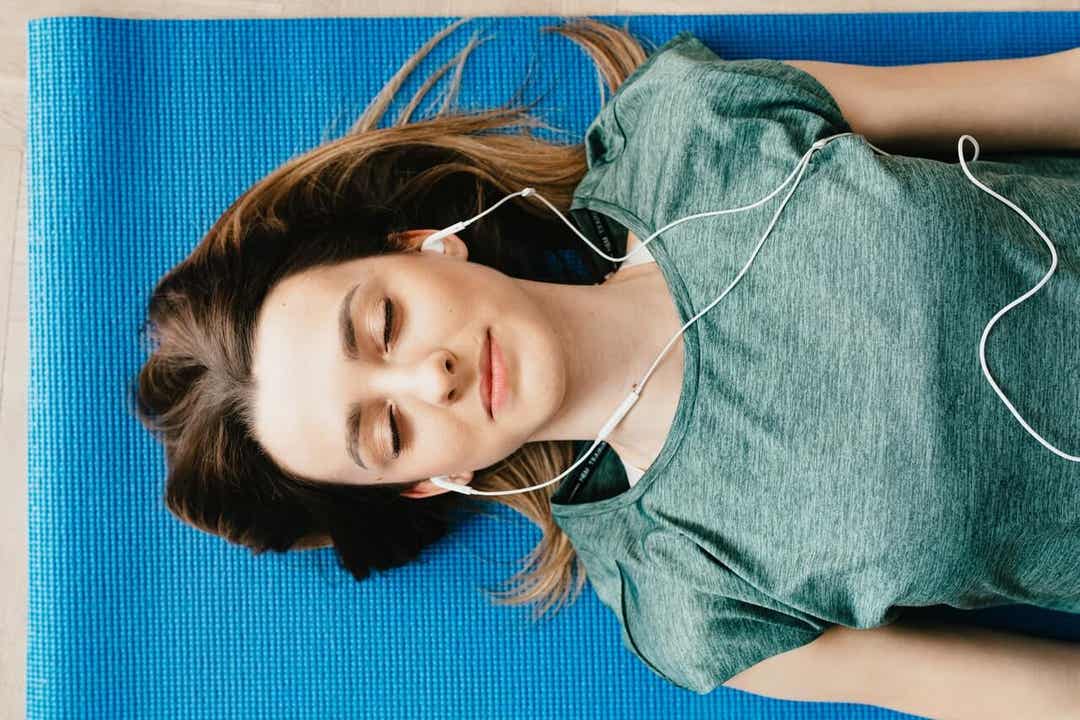Kobieta leżąca na macie z zamkniętymi oczami, słucha muzyki.
