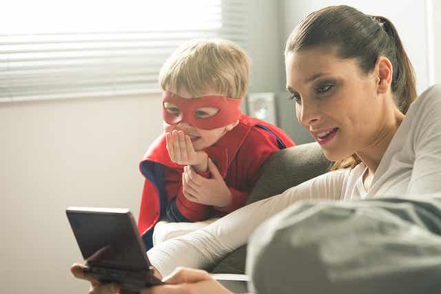 En kvinde, der sidder i sin stue og kigger på en digital enhed med et barn