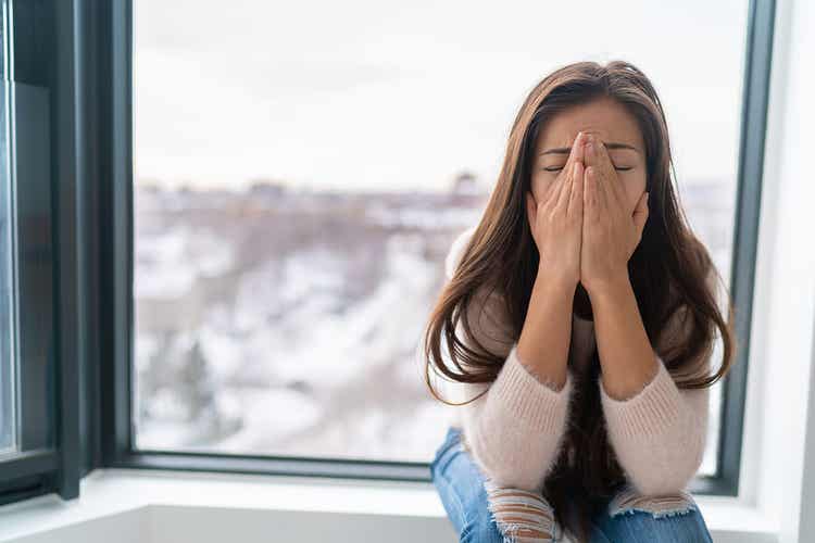 A woman sitting by a window crying.