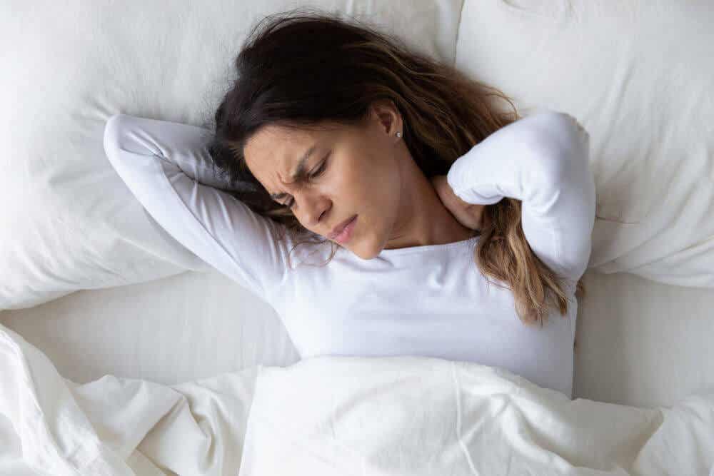A woman lying in bed and holding her neck in pain.
