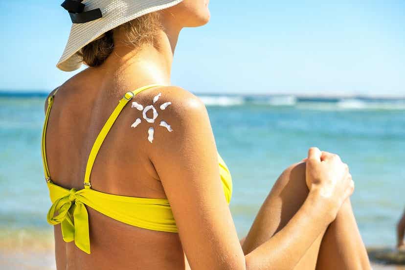 Den Sommer genießen - Eine Frau sitzt am Strand und trägt Sonnencreme.