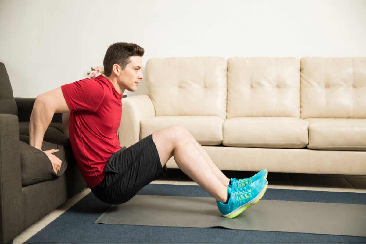 A young man performing tricep dip exercises with his hands on the seat of his couch and his feet on the floor ahead of him.