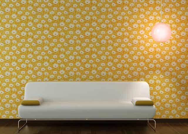 Beyaz çiçekli sarı duvar kağıdıyla kaplı bir duvarın önünde beyaz bir kanepe.
