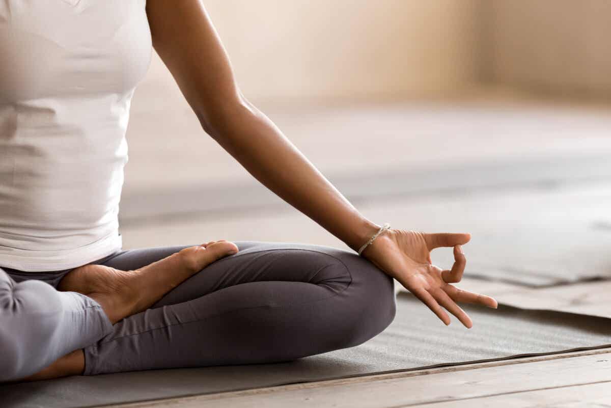 Nærbillede af en kvindes hånd og knæ, mens hun sidder på gulvet og mediterer