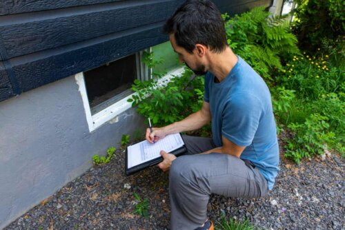 man bending down taking notes on a clipboard about the mold on the house