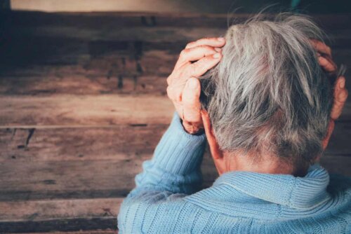 person with their back to the camera and their hands on their head facing a wooden wall short grey hair
