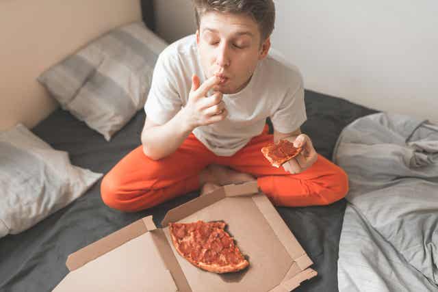En dreng spiser pizza i sengen