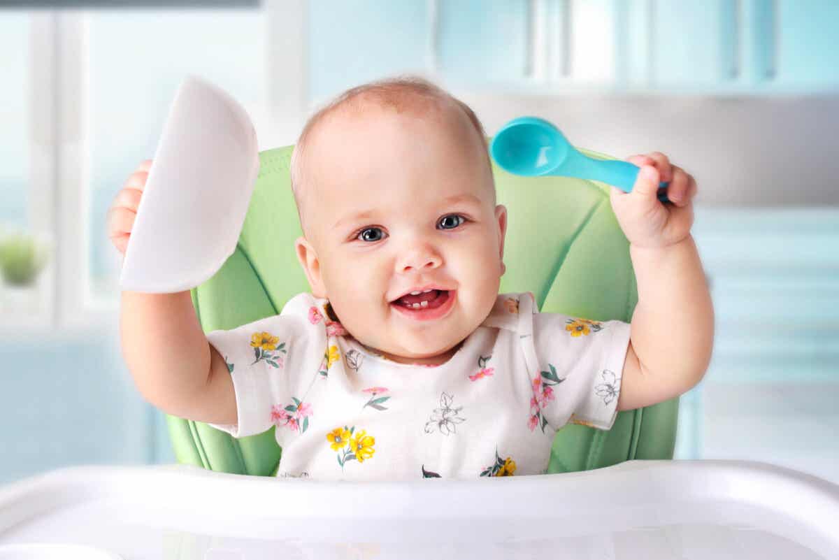 A baby holding her bowl and spoon in the air.