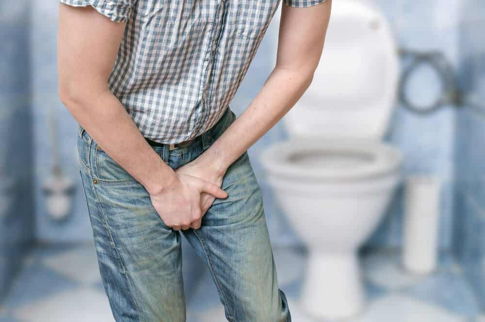 A man standing in the bathroom holding his groin.