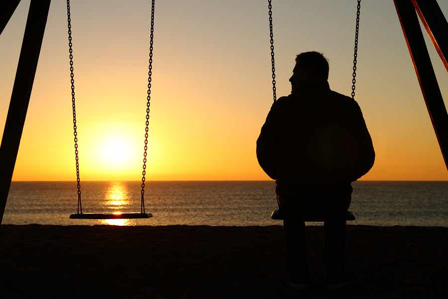 En mann som sitter på en huske og ser på solnedgangen over havet.