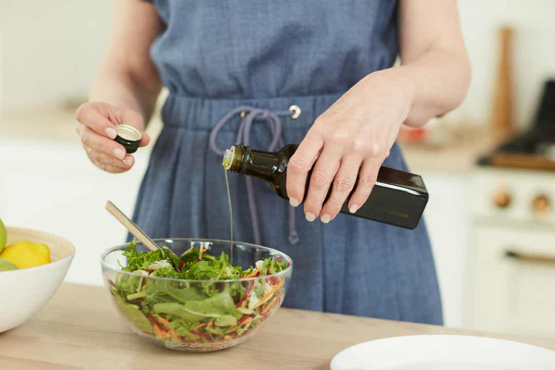 En kvinne som drysser olivenolje på en kastet salat.