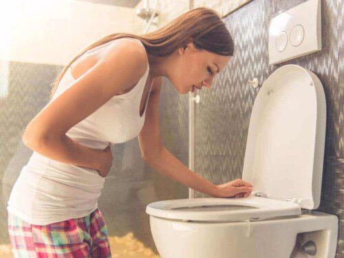Kvinde med morgenkvalme sidder på knæ foran toilet