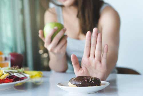 Kvinde med æble i hånden siger nej til donut for at reducere sukker i kosten