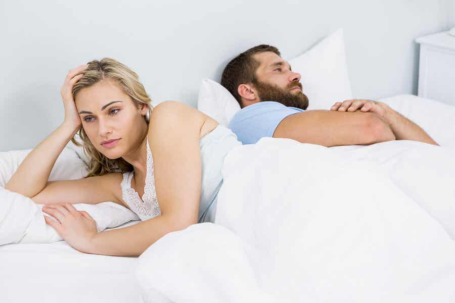 Et par som ligger i sengen med ryggen til hverandre.